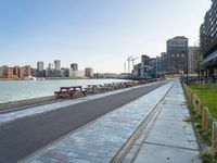 a bench is next to a city river as people walk by the shore line and some buildings