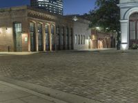 a building with a brick road in front of it, lit up at night, in the distance is the lamp tower