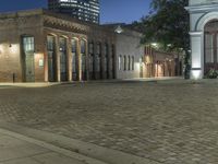 a building with a brick road in front of it, lit up at night, in the distance is the lamp tower