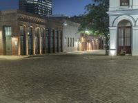 a building with a brick road in front of it, lit up at night, in the distance is the lamp tower