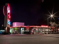 a large restaurant with neon signs lit up in the dark time by street lights and parking lot