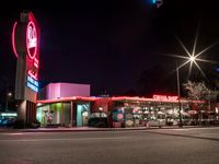 a large restaurant with neon signs lit up in the dark time by street lights and parking lot