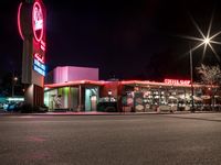 a large restaurant with neon signs lit up in the dark time by street lights and parking lot