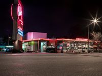 a large restaurant with neon signs lit up in the dark time by street lights and parking lot