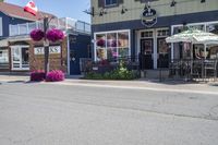 a restaurant with flowers outside on a sidewalk and with several windows there is a restaurant, an outdoor cafe, a restaurant tent and chairs