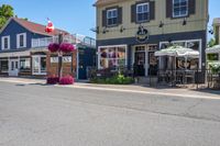 a restaurant with flowers outside on a sidewalk and with several windows there is a restaurant, an outdoor cafe, a restaurant tent and chairs