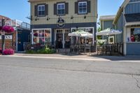a restaurant with flowers outside on a sidewalk and with several windows there is a restaurant, an outdoor cafe, a restaurant tent and chairs