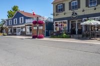 a restaurant with flowers outside on a sidewalk and with several windows there is a restaurant, an outdoor cafe, a restaurant tent and chairs
