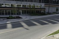 the shadows of a person riding a bike past a building on the street while there is an empty sidewalk in front of them