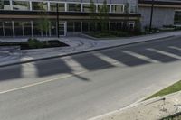 the shadows of a person riding a bike past a building on the street while there is an empty sidewalk in front of them