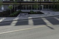 the shadows of a person riding a bike past a building on the street while there is an empty sidewalk in front of them