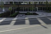 the shadows of a person riding a bike past a building on the street while there is an empty sidewalk in front of them