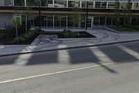 the shadows of a person riding a bike past a building on the street while there is an empty sidewalk in front of them