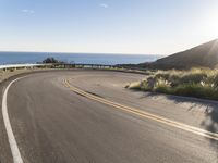 a motorcycle is going down the winding road near the ocean and sky on an autumn day