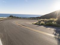 a motorcycle is going down the winding road near the ocean and sky on an autumn day