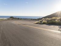 a motorcycle is going down the winding road near the ocean and sky on an autumn day