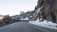 a man riding a motorcycle down the side of a road near a cliff in the snow