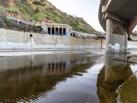 a river flowing underneath an overpass in a rural area in europe and italy, with large structures visible in the background