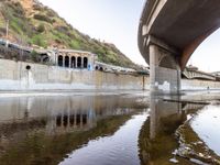 a river flowing underneath an overpass in a rural area in europe and italy, with large structures visible in the background