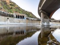 a river flowing underneath an overpass in a rural area in europe and italy, with large structures visible in the background