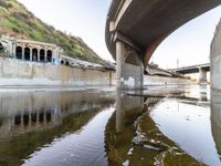 a river flowing underneath an overpass in a rural area in europe and italy, with large structures visible in the background