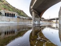 a river flowing underneath an overpass in a rural area in europe and italy, with large structures visible in the background