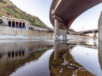 a river flowing underneath an overpass in a rural area in europe and italy, with large structures visible in the background