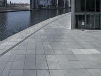 view of a walkway in front of the building and lake side water with a glass fronted building in the back