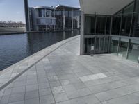 view of a walkway in front of the building and lake side water with a glass fronted building in the back