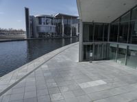 view of a walkway in front of the building and lake side water with a glass fronted building in the back