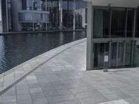 view of a walkway in front of the building and lake side water with a glass fronted building in the back