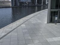 view of a walkway in front of the building and lake side water with a glass fronted building in the back