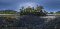 a big pile of dirt sitting next to a river and forest area filled with trees