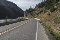 a roadway next to a river with mountain in the distance and trees on the side of the road