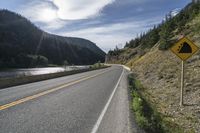 a roadway next to a river with mountain in the distance and trees on the side of the road