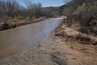 a small river next to the highway in the mountains where the road is flooded with water