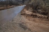 a small river next to the highway in the mountains where the road is flooded with water