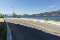 an empty roadway near a lake and a bridge on a sunny day with some trees