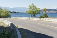 an empty roadway near a lake and a bridge on a sunny day with some trees