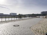 view of an empty walkway along the river with a bridge in the background and several buildings across it