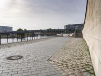 view of an empty walkway along the river with a bridge in the background and several buildings across it