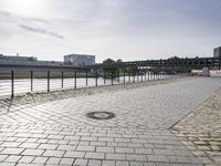 view of an empty walkway along the river with a bridge in the background and several buildings across it