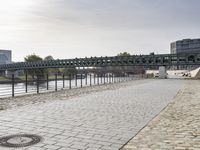 view of an empty walkway along the river with a bridge in the background and several buildings across it