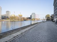 a brick road along a river near tall buildings with red brick sidewalking on the side