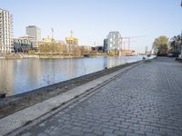 a brick road along a river near tall buildings with red brick sidewalking on the side