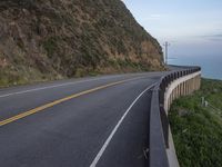 a man is on a motorcycle riding by the road near the ocean and a cliff