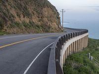 a man is on a motorcycle riding by the road near the ocean and a cliff