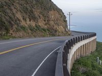 a man is on a motorcycle riding by the road near the ocean and a cliff