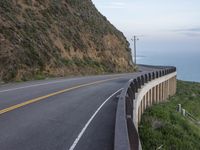 a man is on a motorcycle riding by the road near the ocean and a cliff