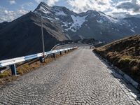 a cobbled road runs along a narrow side of a mountain range with mountains in the background